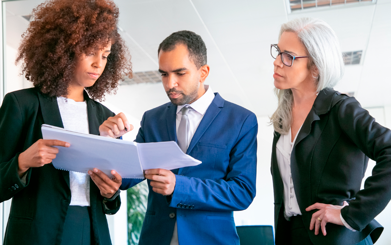 Capa de blog post sobre due diligence em trabalho temporário. Na imagem, há três pessoas diversas. Elas avaliam documentos em conjunto.