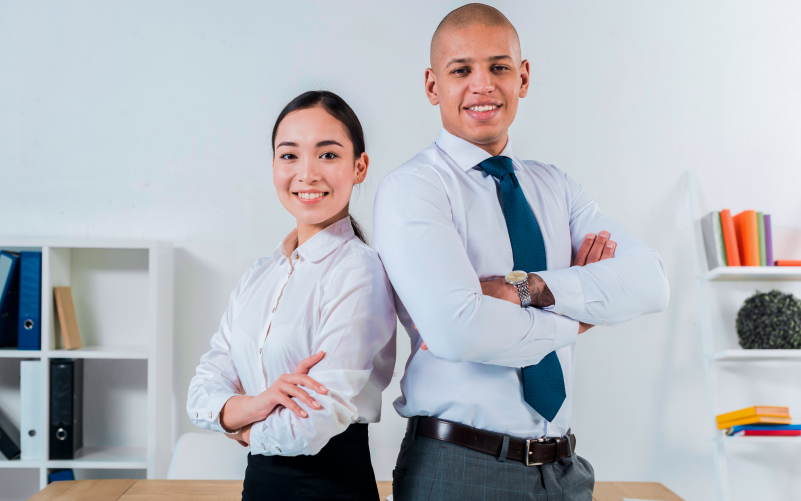 Imagem de capa de blog post sobre contratar aprendiz. Na foto, há um líder e uma jovem aprendiz, ambos de braços cruzados, sorrindo e vestidos formalmente em um ambiente corporativo.